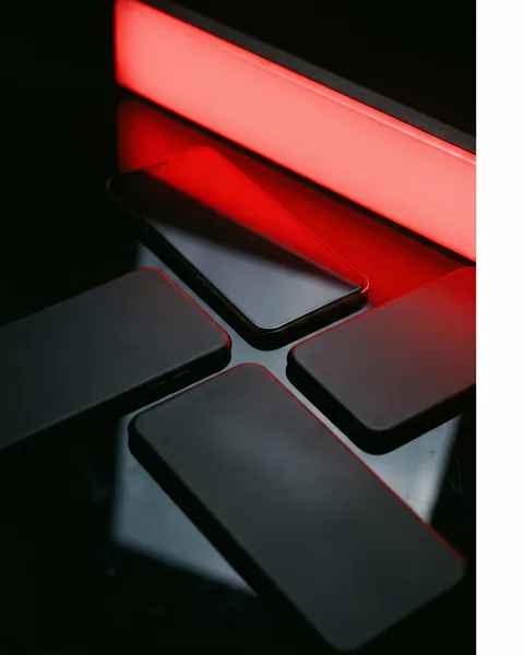 Four phones on black glass, one face-up reflecting the red light.